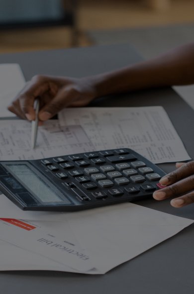 A woman's hands rest on a calculator and papers, indicating a moment of calculation or financial planning.