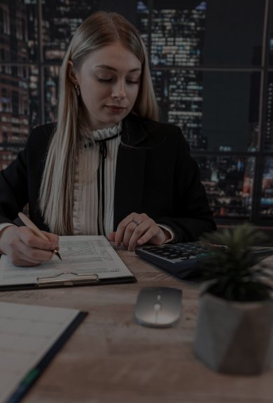 A woman dressed in a business suit is focused on writing on a piece of paper, embodying a dedicated work ethic.